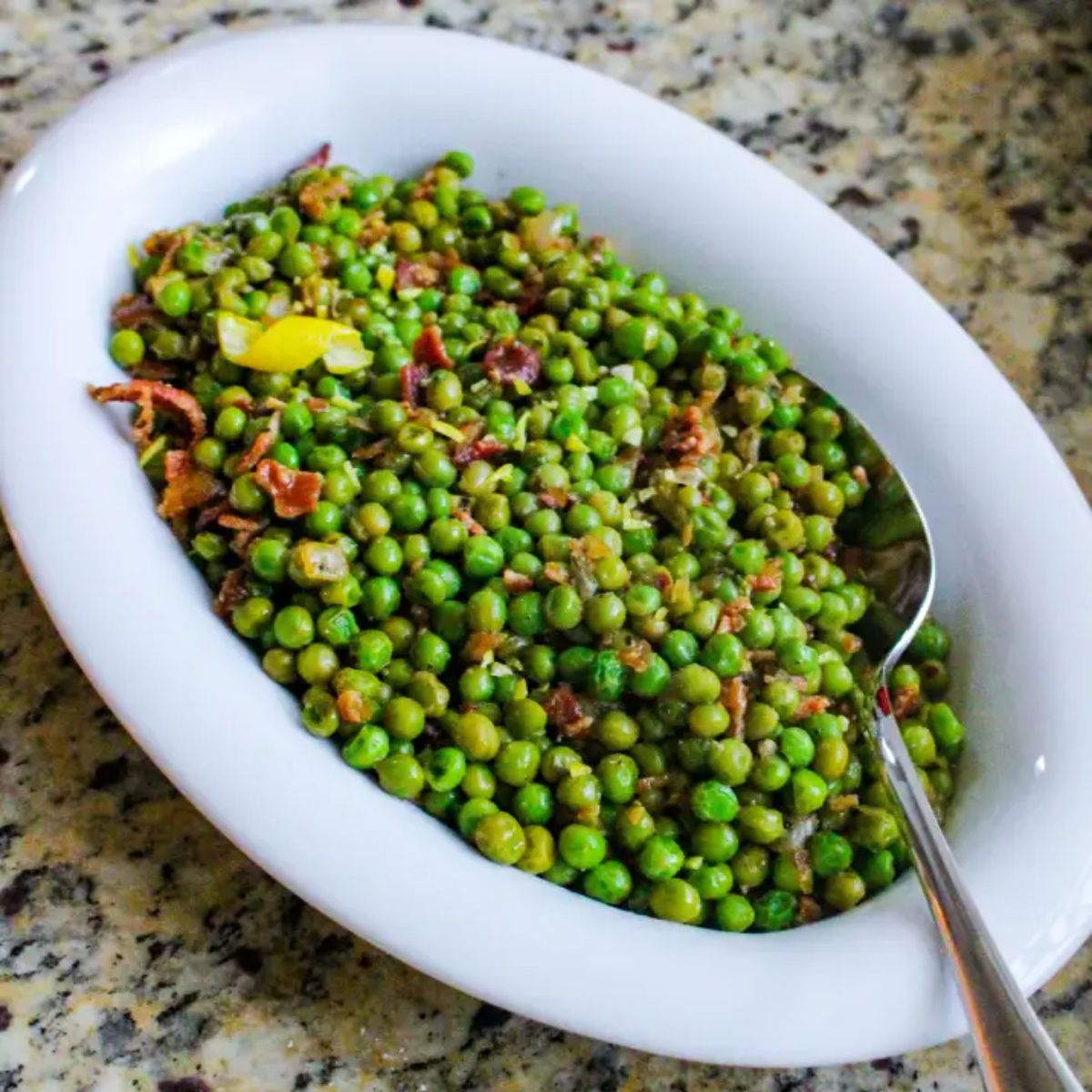 Healthy lemon bacon peas in a white bowl with a spoon.