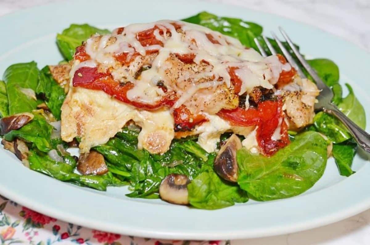 Scrumptious stuffed chicken breasts italian style with salad on a white plate with a fork.