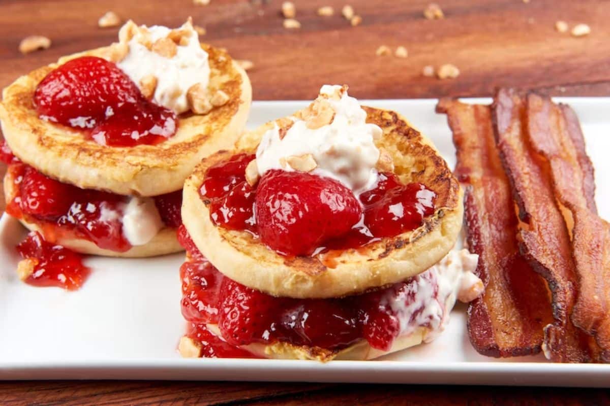 Juicy strawberry shortcake french toasts on a white tray with slices of bacon.
