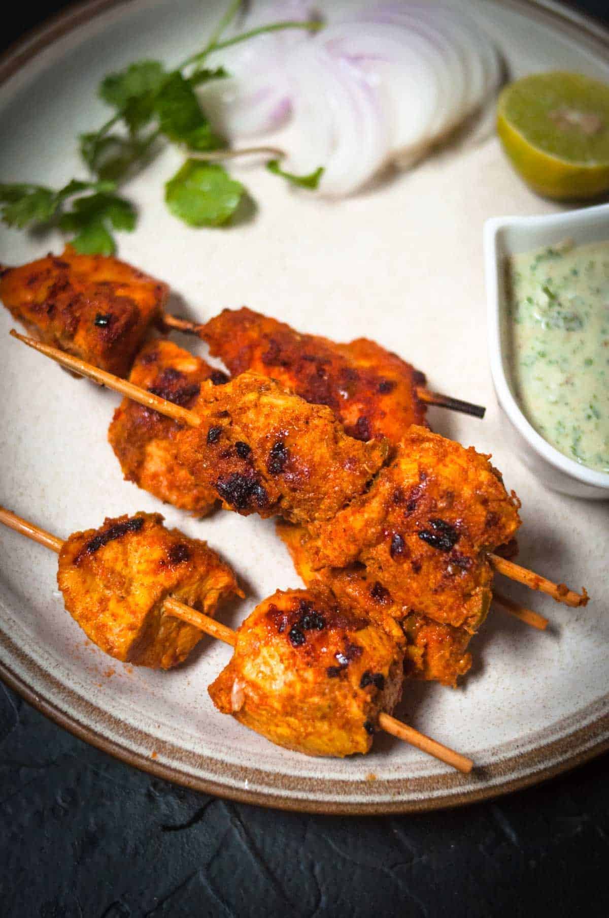 Mouth-watering chicken boti kebabs on a white tray with a bowl of dip.