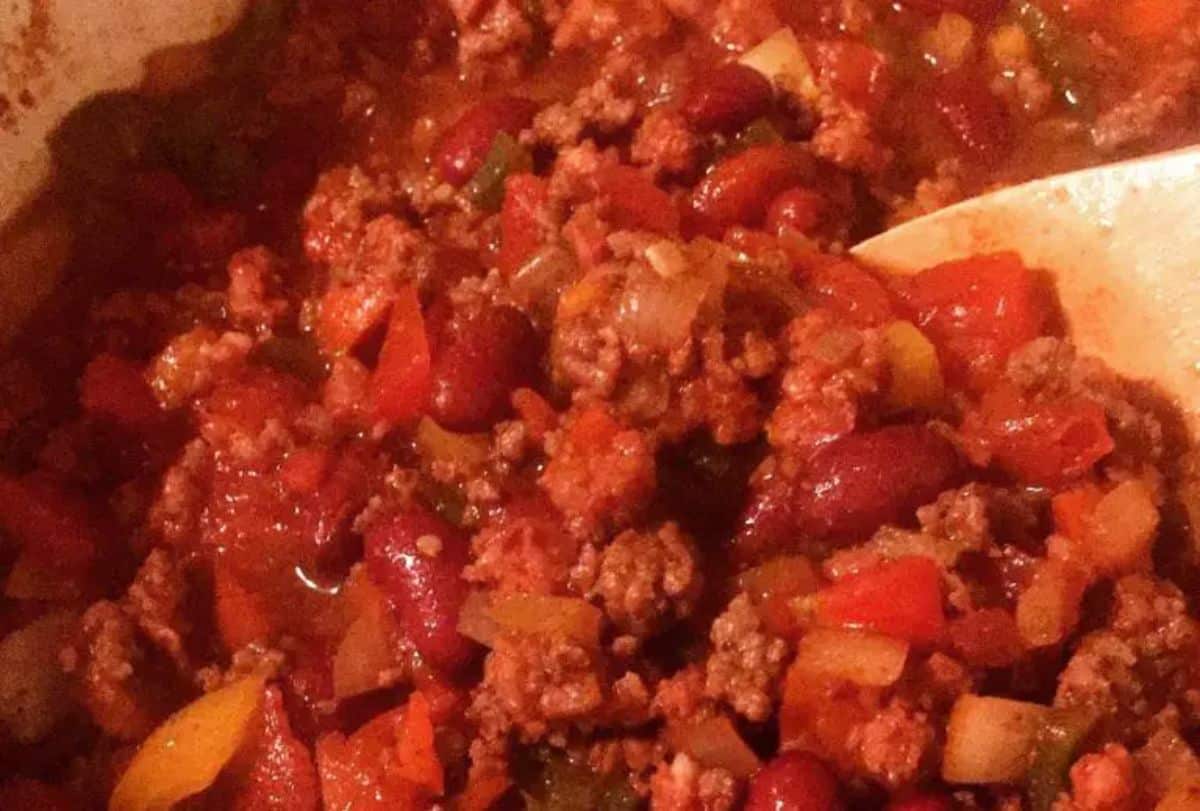 Flavorful andouille sausage and ground beef chili in a bowl with a wooden spoon.