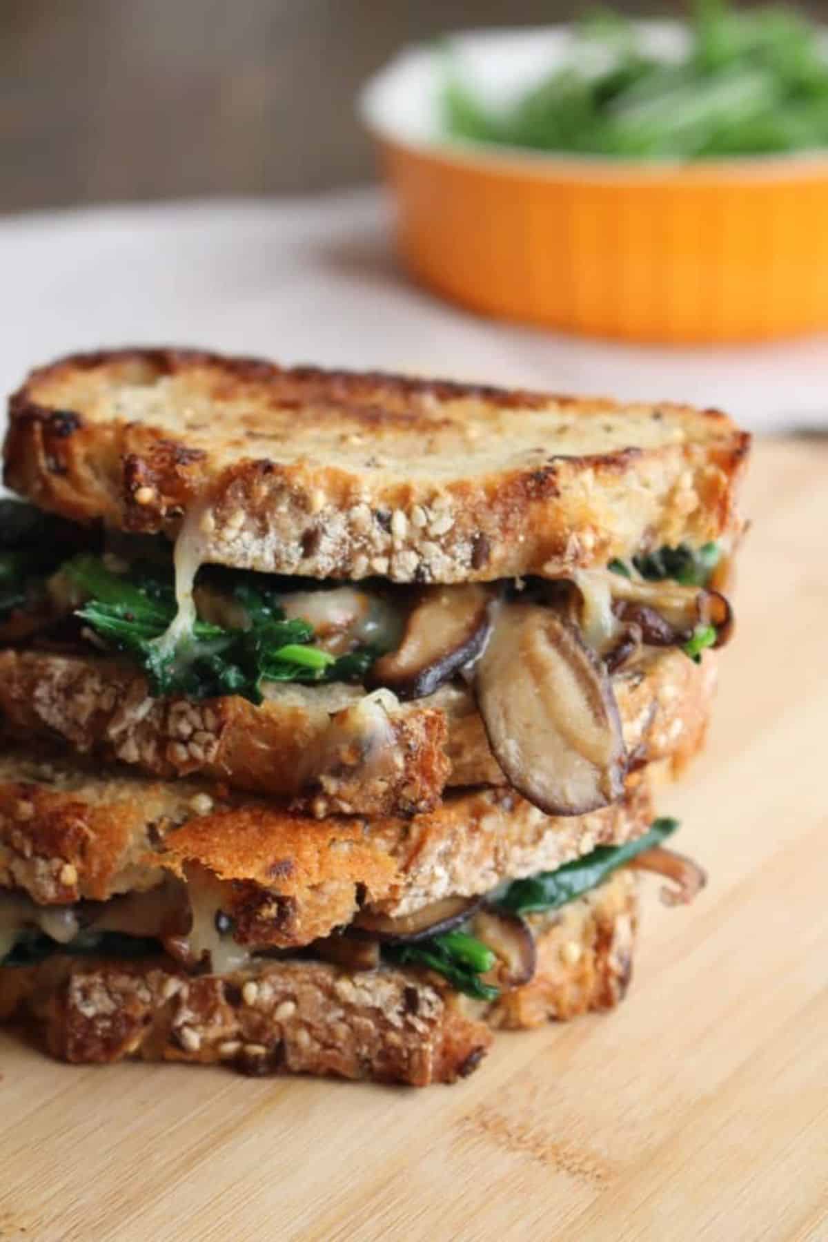 A pile of mouth-watering mushroom grilled cheese melts on a wooden tray.
