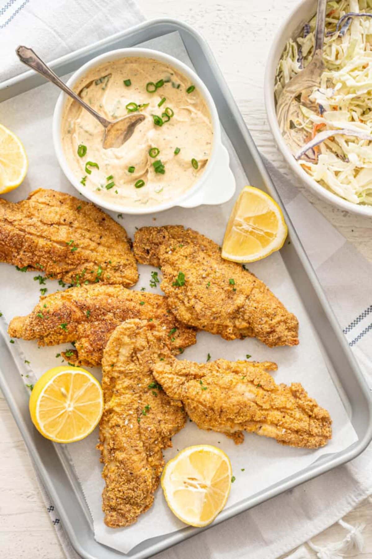 Crunchy fried catfish with lemon and a bowl of condiment on a tray.