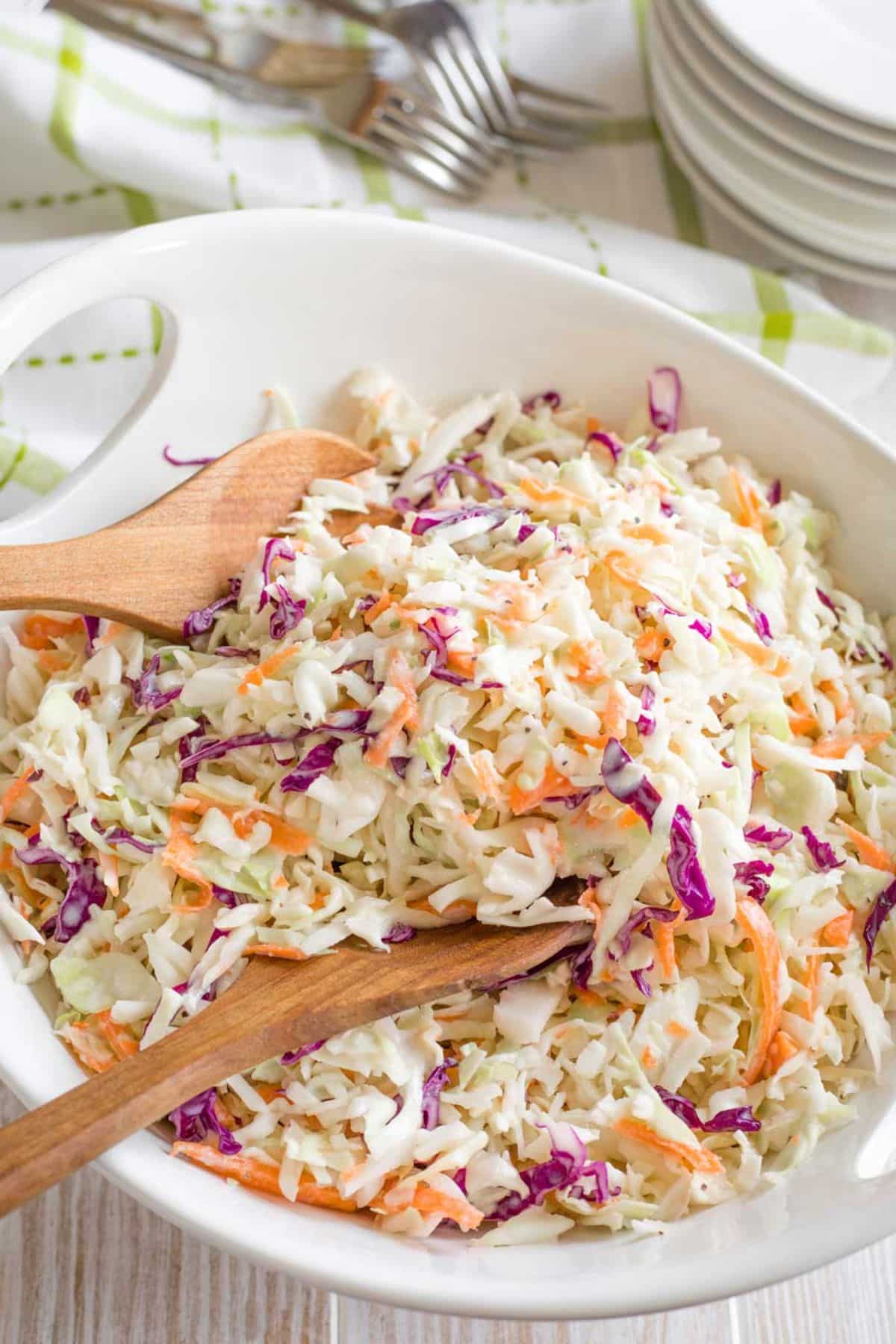 Healthy greek yogurt coleslaw in a white bowl with two wooden spoons.