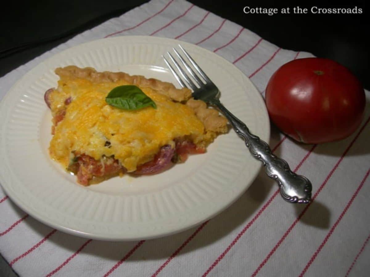 A piece of tomato pie on a white plate with a fork.