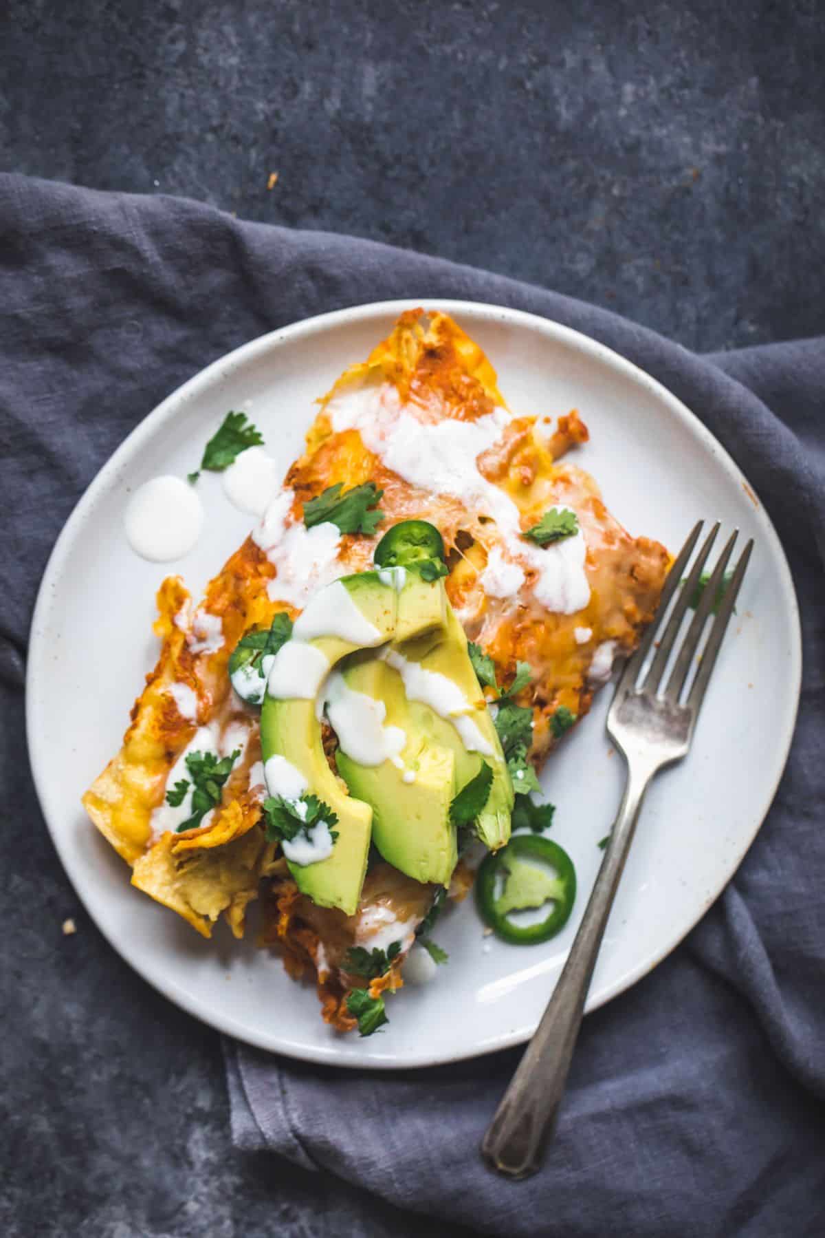 Flavorful spicy black bean chicken enchiladas on a white plate with a fork.