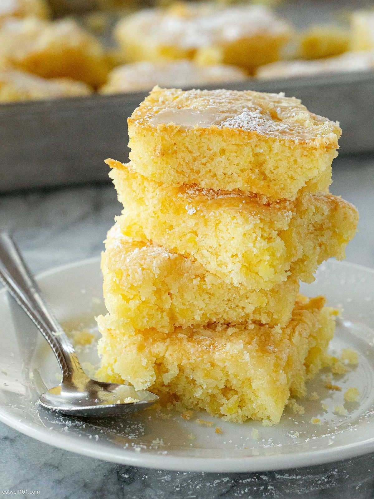 A pile of coconut drizzle pineapple barson a gray plate with a spoon.