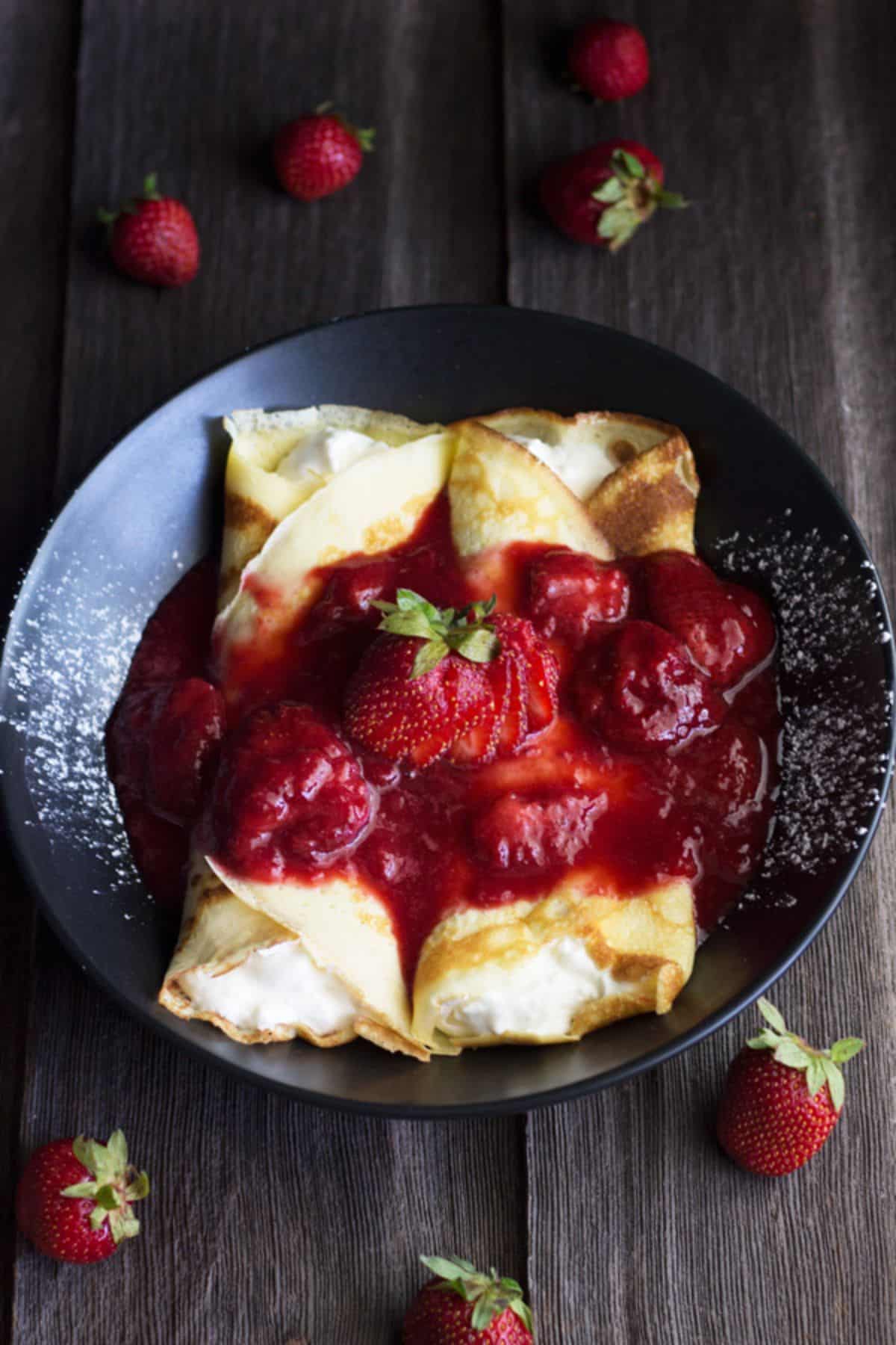 Mouth-watering strawberry cream crepes on a black plate.