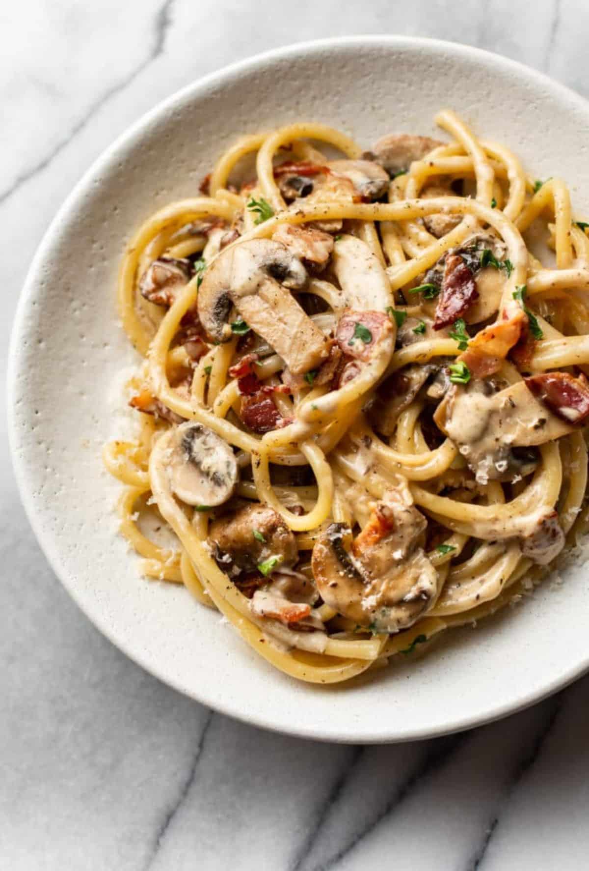 Flavorful bacon mushroom pasta on a white plate.