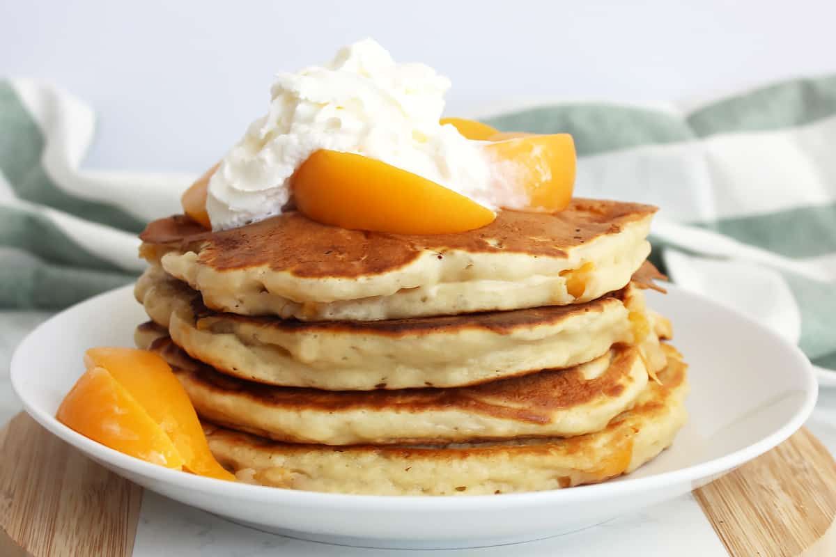A pile of scrumptious peach pancakes on a white plate.