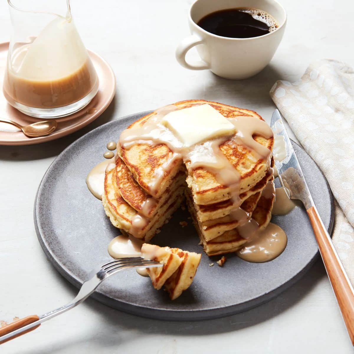 A pile of sour cream pancakes with sour-cream maple syrup on a gray plate with cutlery.