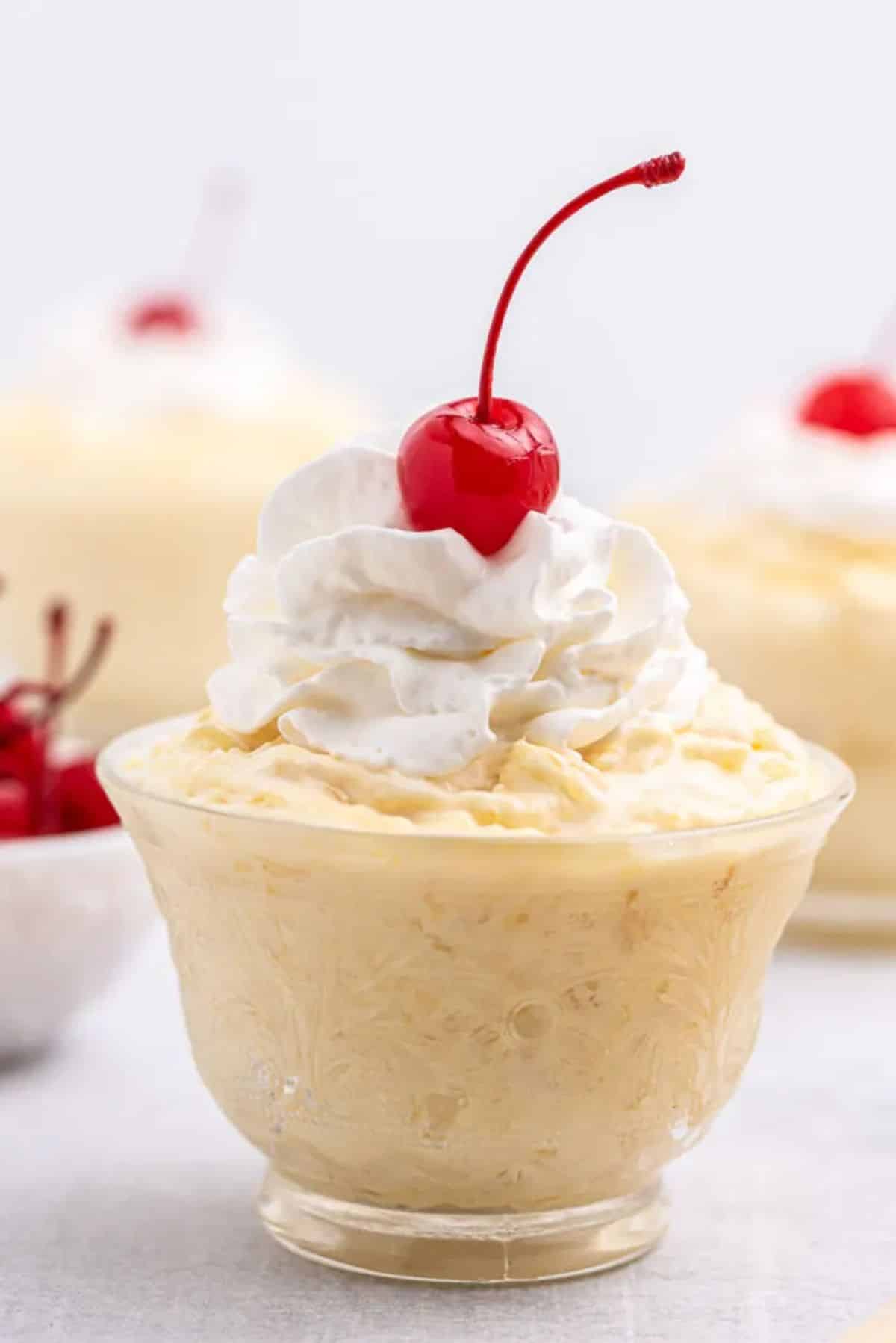 Creamy pineapple parfait garnished with cherry in a glass bowl.