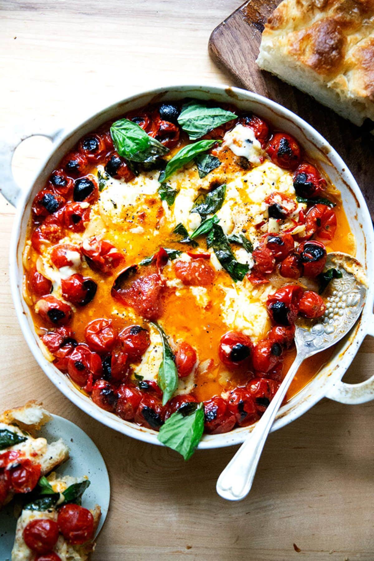 Scrumptious baked feta with cherry tomatoes in a skillet with a spoon.