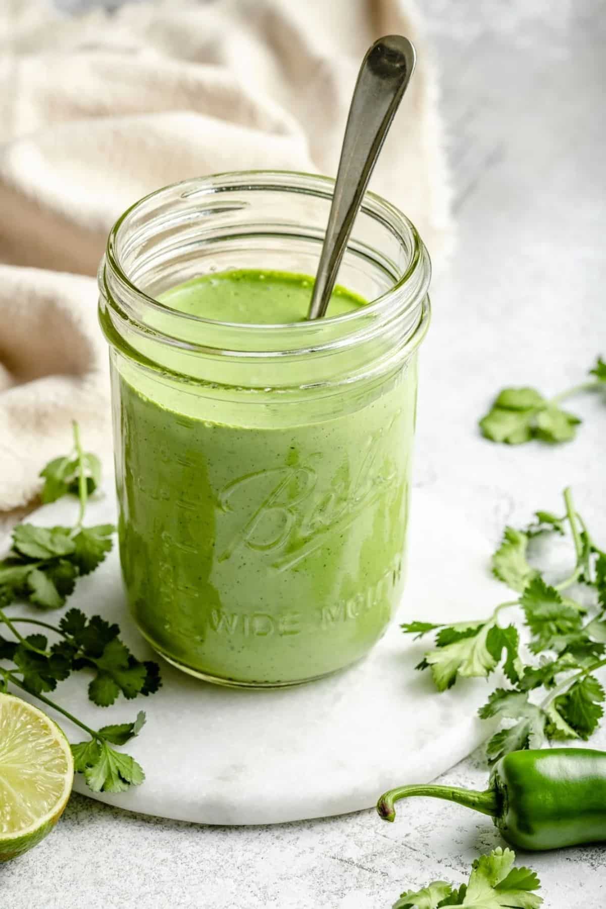 Healthy spicy cilantro yogurt sauce in a glass jar with a spoon.