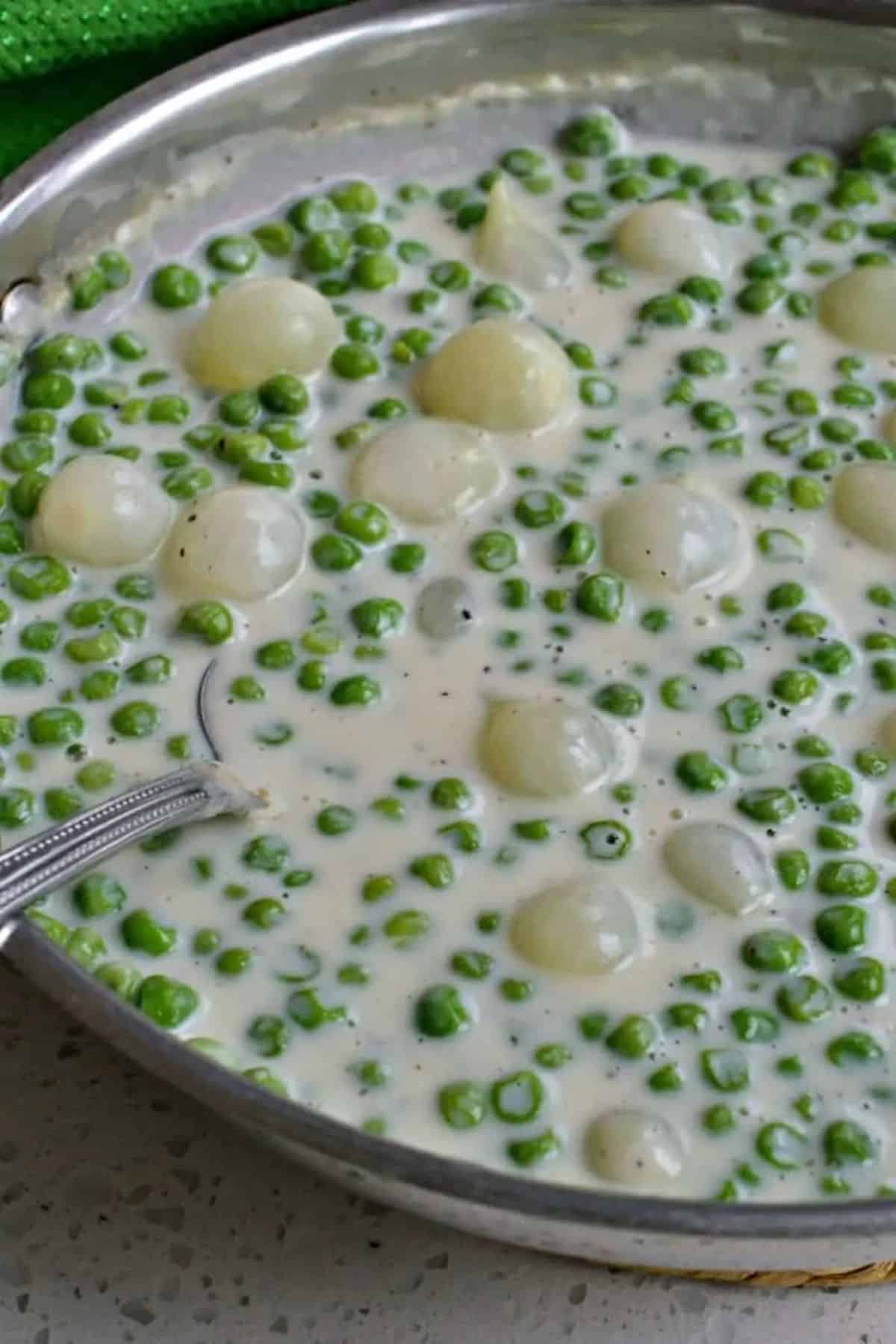 Flavorful creamed peas in a metal bowl with a spoon.