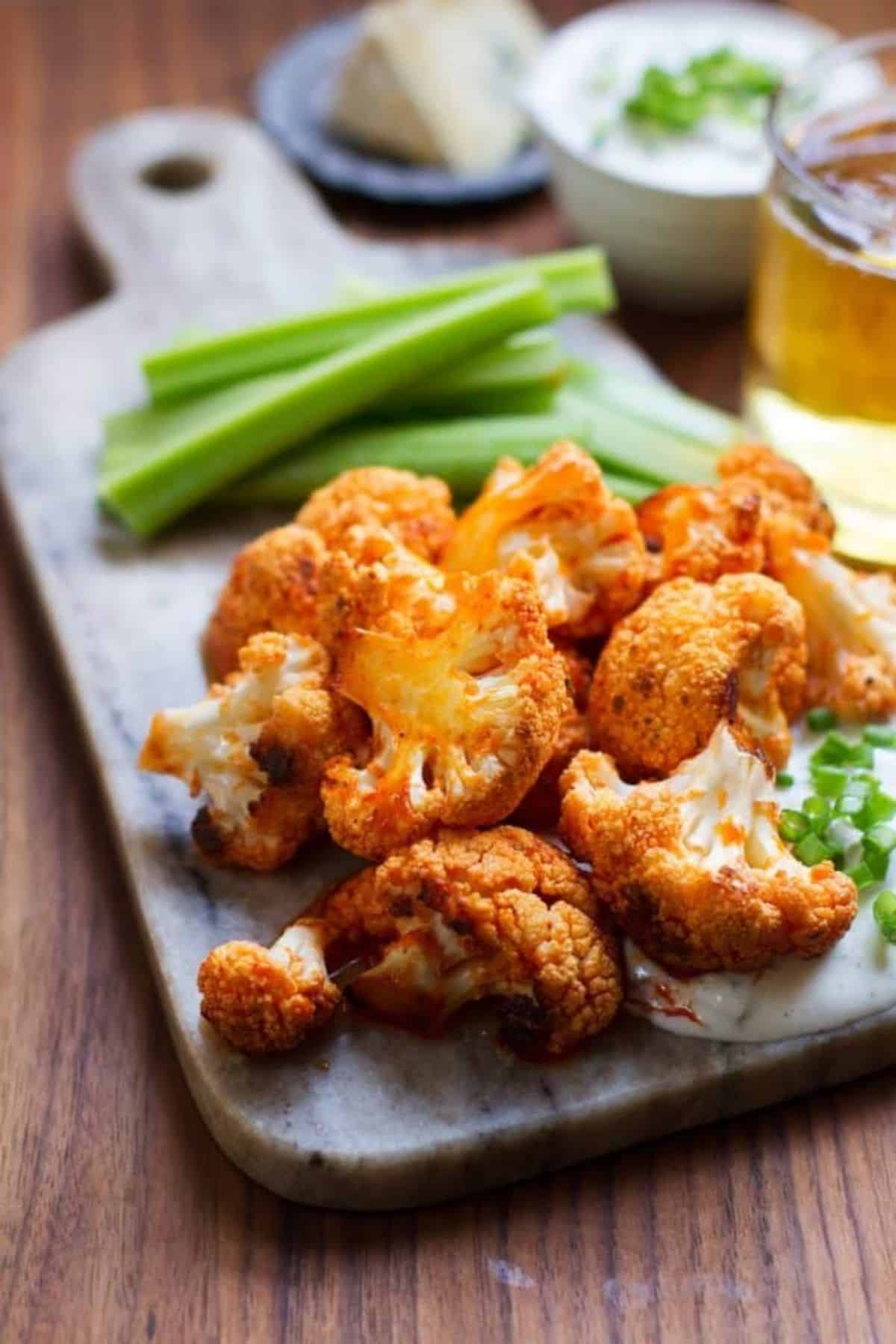 Crispy buffalo cauliflower with blue cheese dressing on a wooden cutting board.