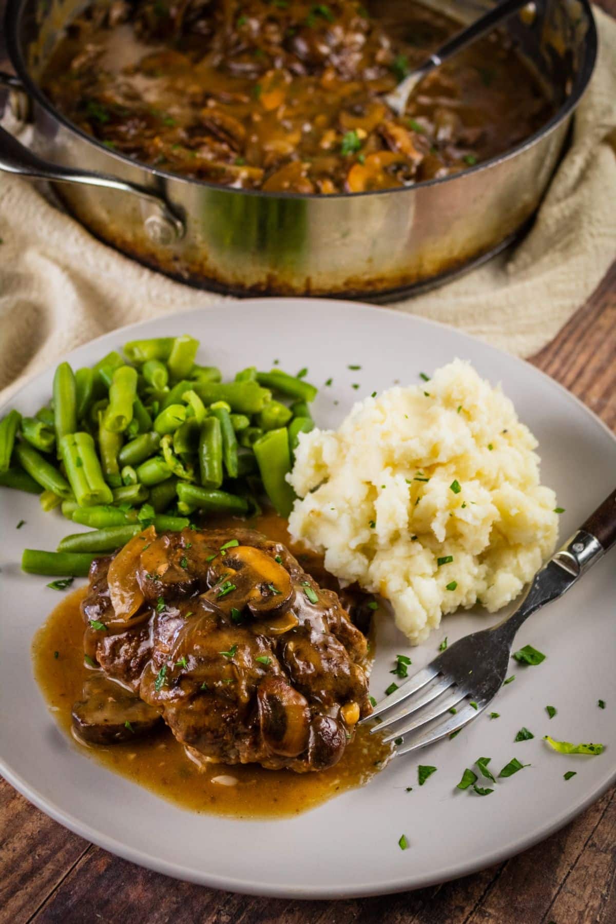 Juicy salisbury steak with mashed potatoes, beans on a white plate with a fork.