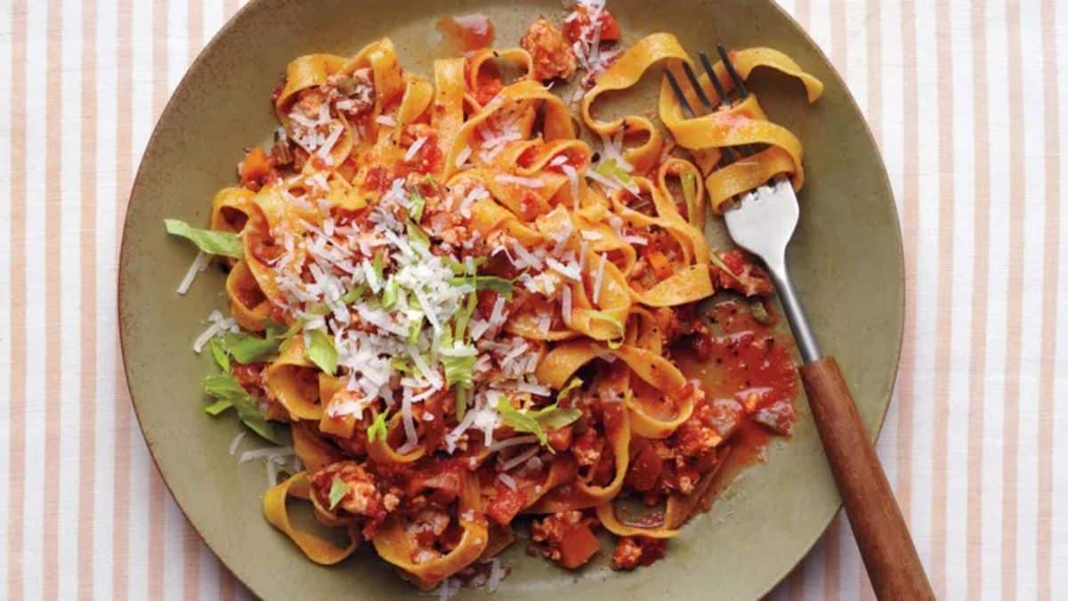 Mouth-watering chicken bolognese with tagliatelle on a gray plate with a fork.
