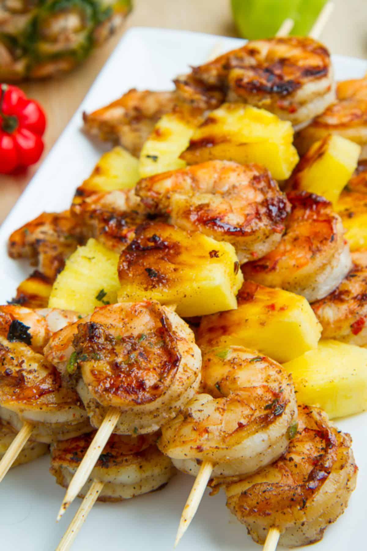 Mouth-watering grilled jerk shrimp and pineapple skewers on a white tray.