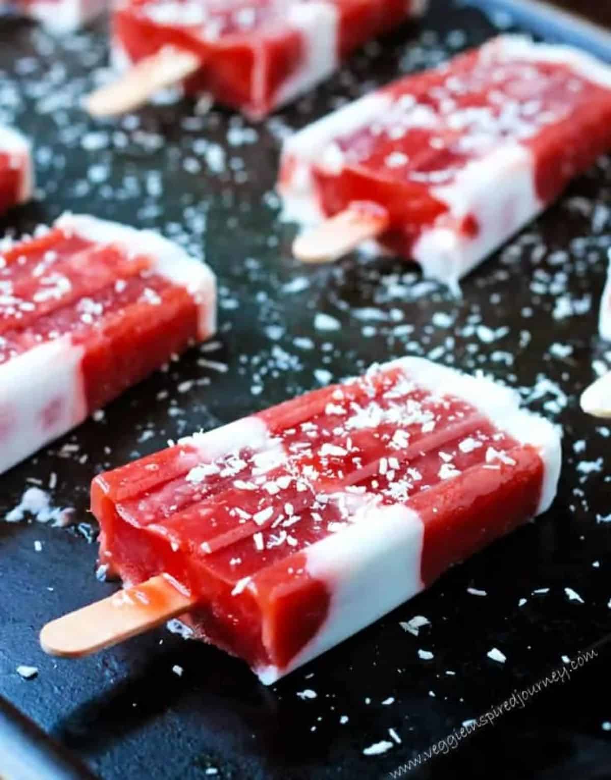 Fresh strawberry coconut rhubarb popsicles on a black tray.