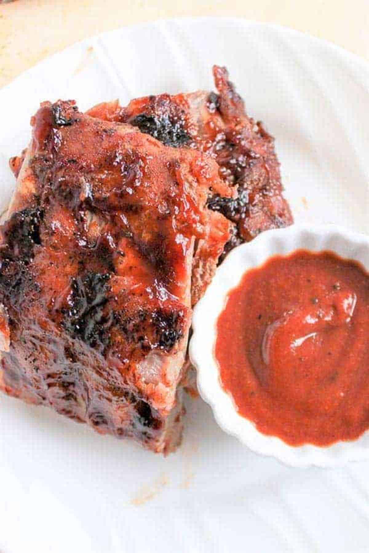 Juicy easy grilled baby back pork ribs with a bowl of dip on a plate.