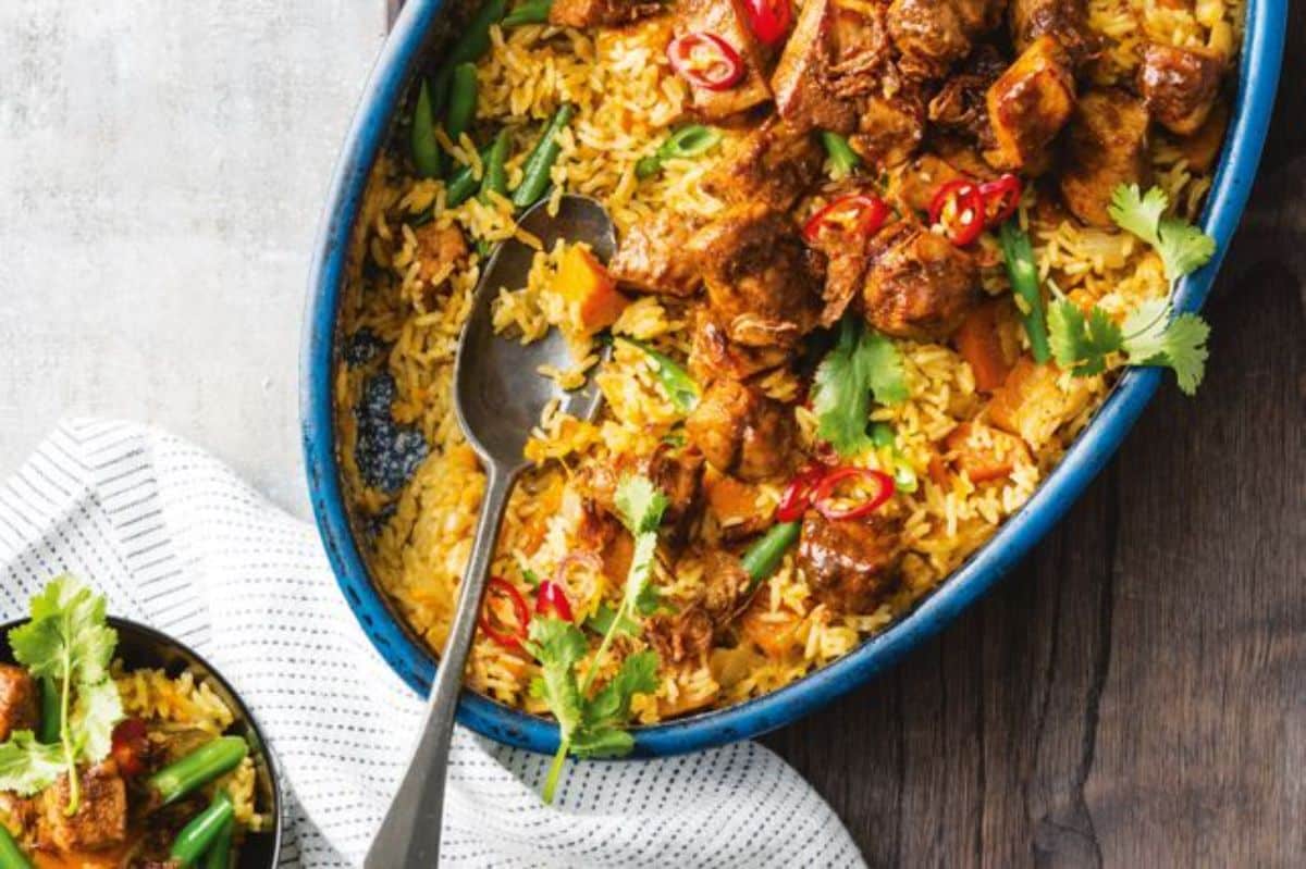 Mouth-watering one-pan yellow pork curry with coconut rice in a blue casserole.