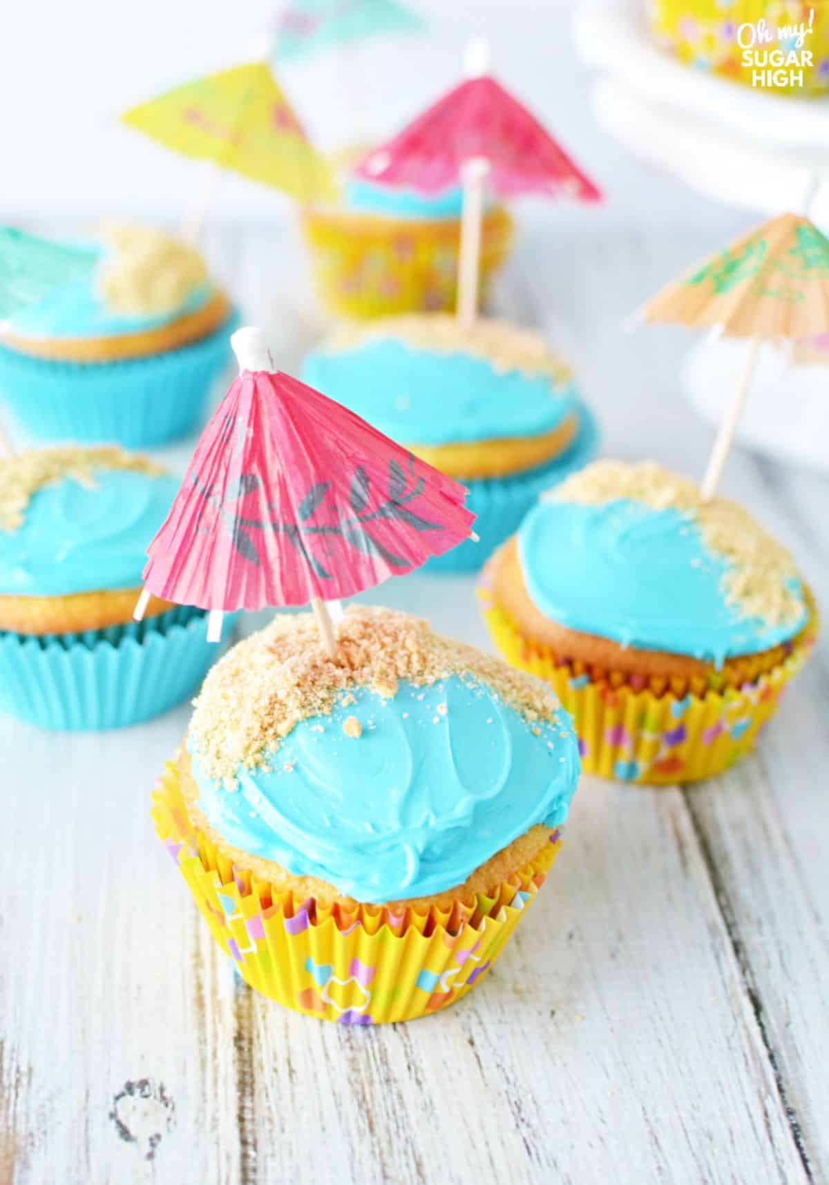 Mouth-watering umbrella cupcakes on a wooden table.