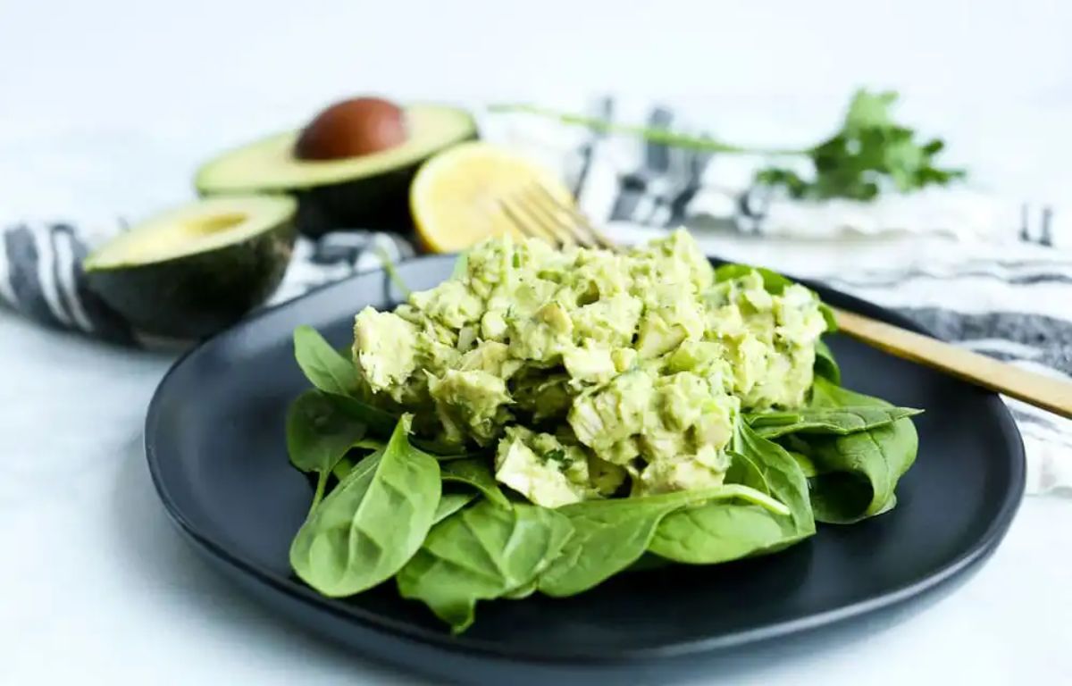 Healthy avocado chicken salad on a black plate with a fork.