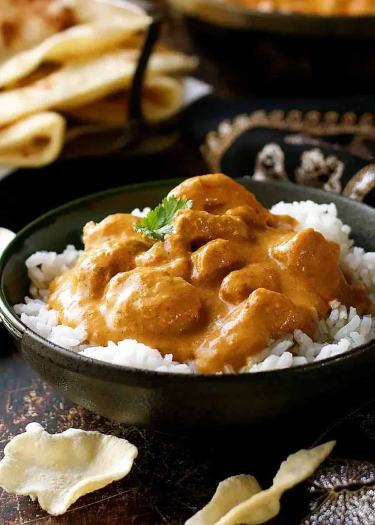 Juicy butter chicken with rice in a black bowl.