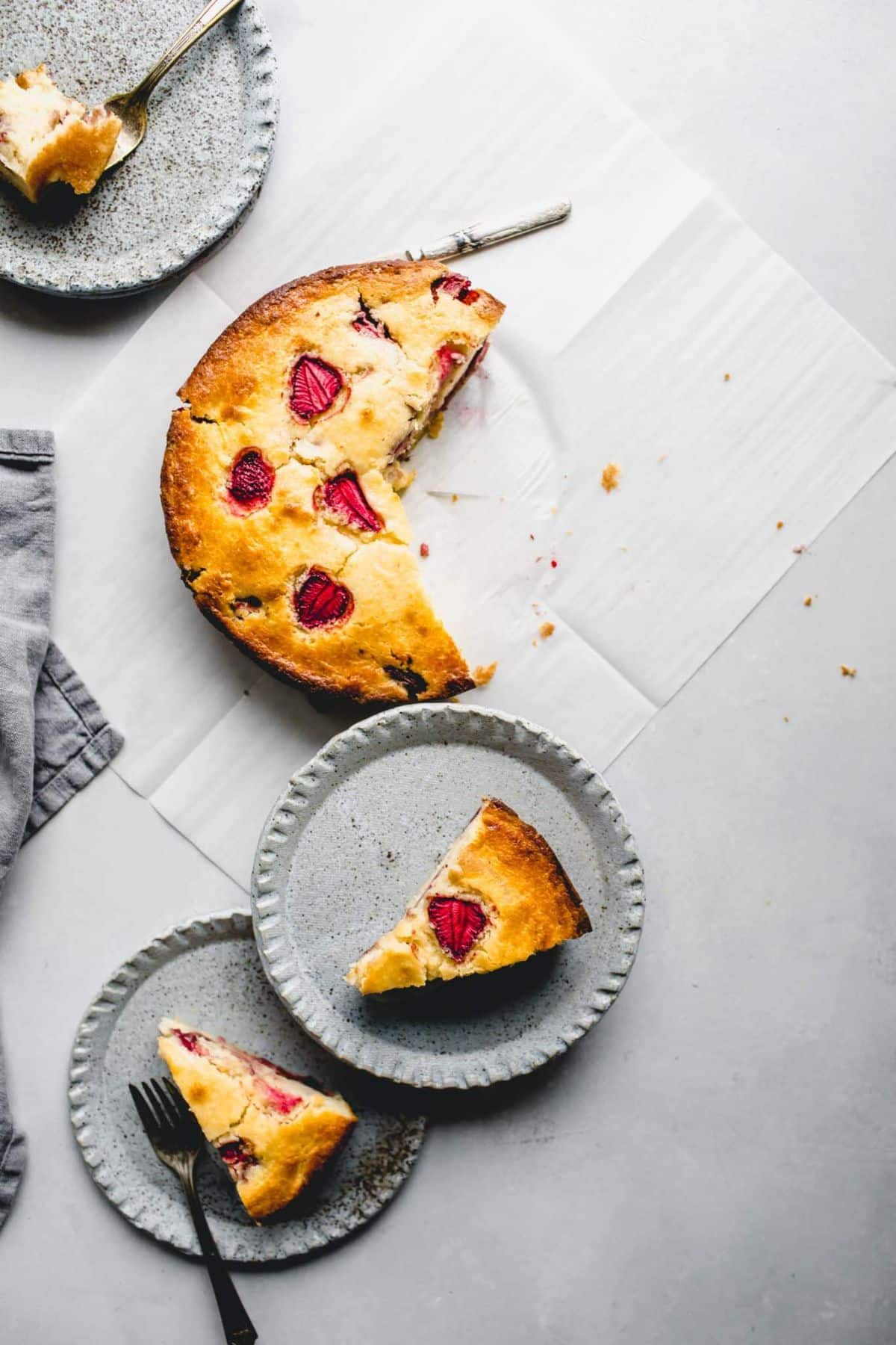 Delicious strawberry ricotta cake on a table and slices on gray plates.