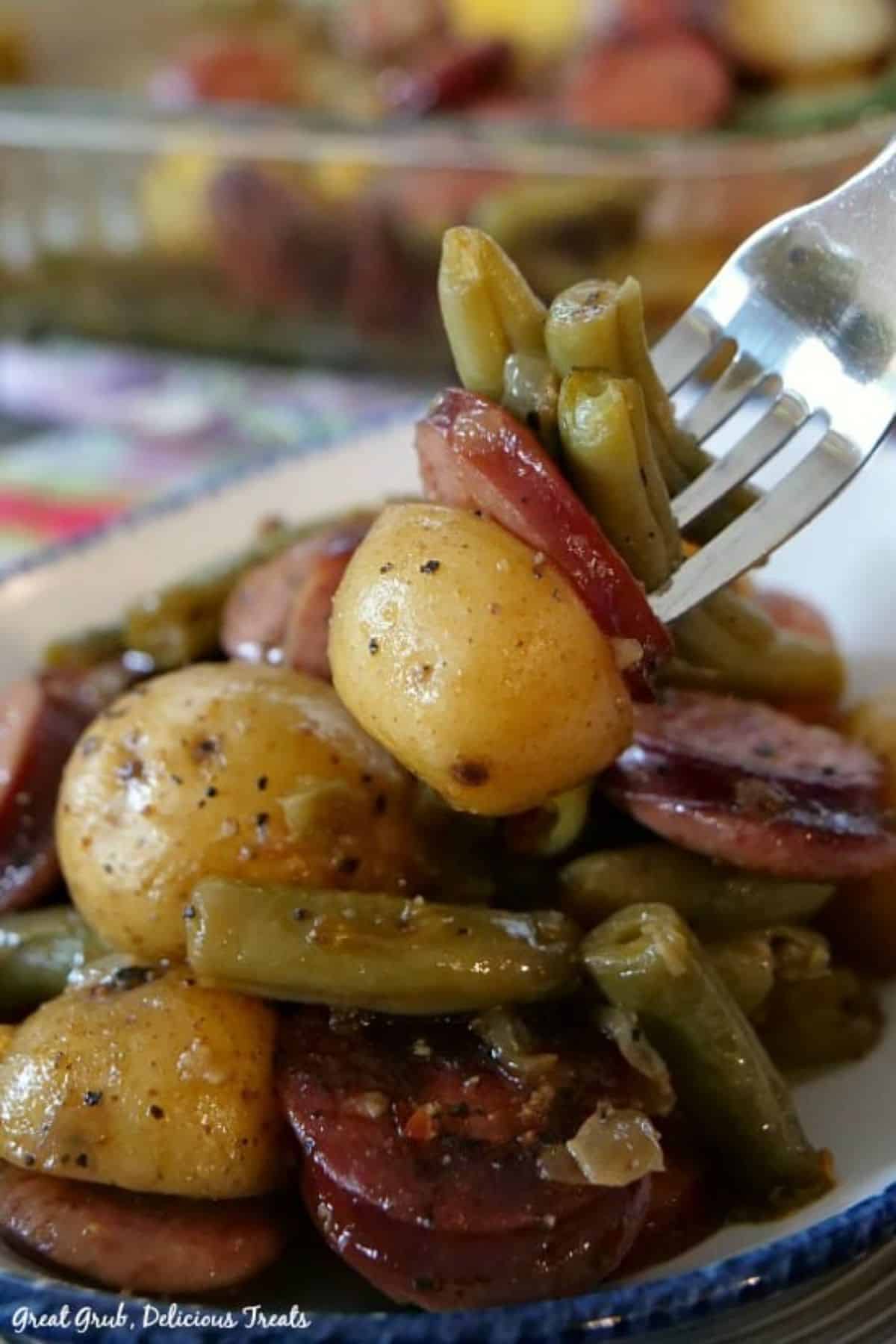 Juicy sausagem green beans and potatoes picked by a fork.