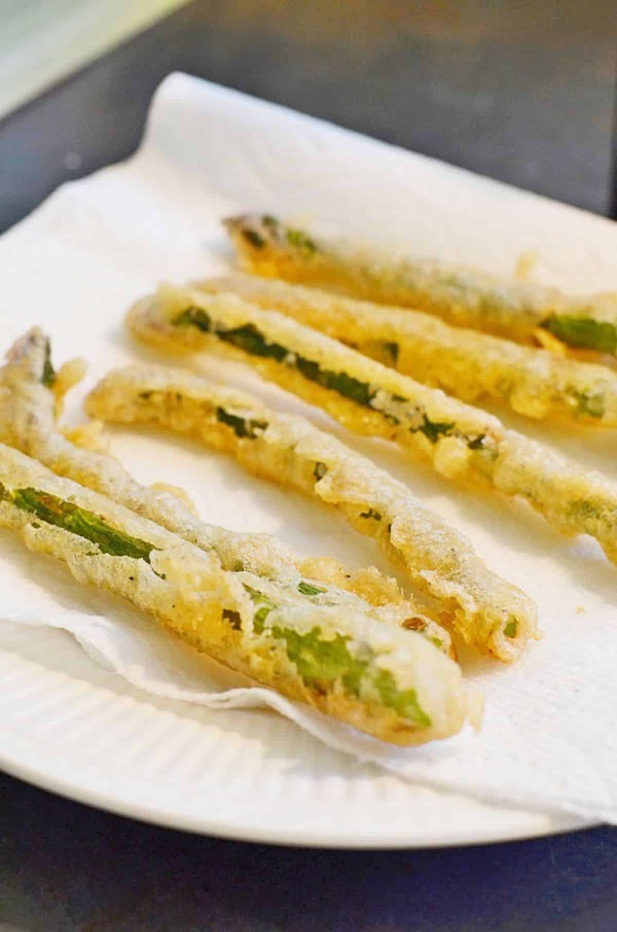 Crispy fried asparagus with spicy dipping sauce on a white plate.