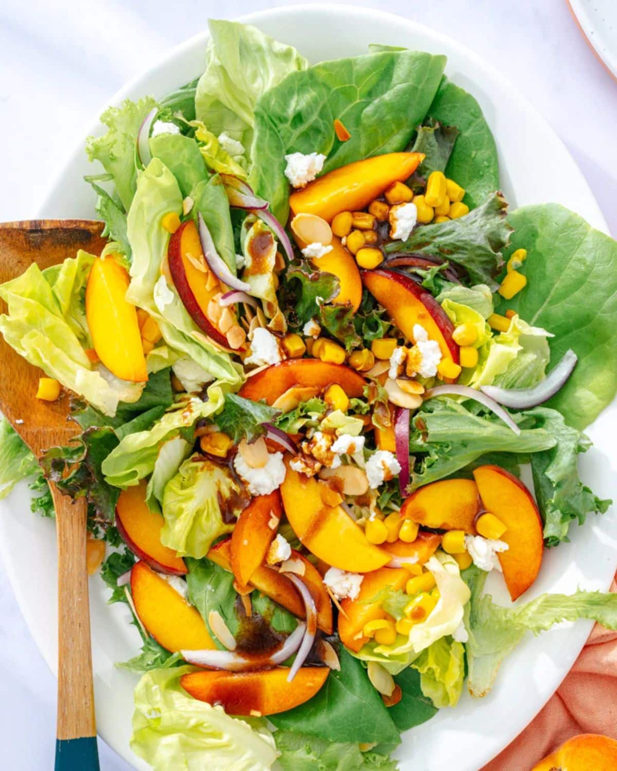 Healthy peach salad on a white tray with a wooden spoon.