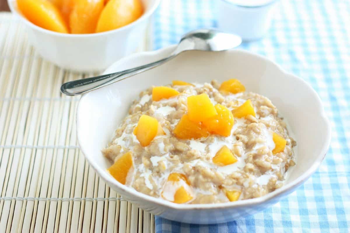 Healthy peaches and cream oatmeal in a white bowl with a spoon.