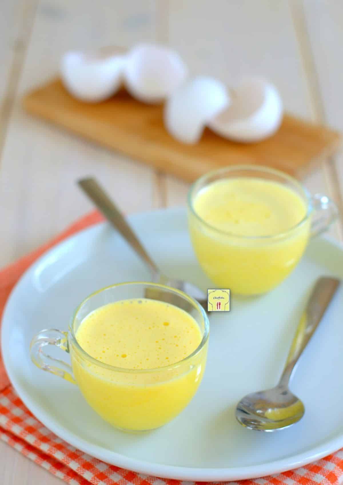 Fresh uovo sbattuto dessert in two glass cups on a blue plate with two spoons.