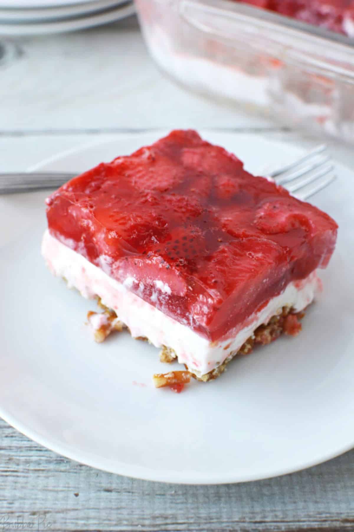 A piece of strawberry pretzel salad on a white plate with a spoon.