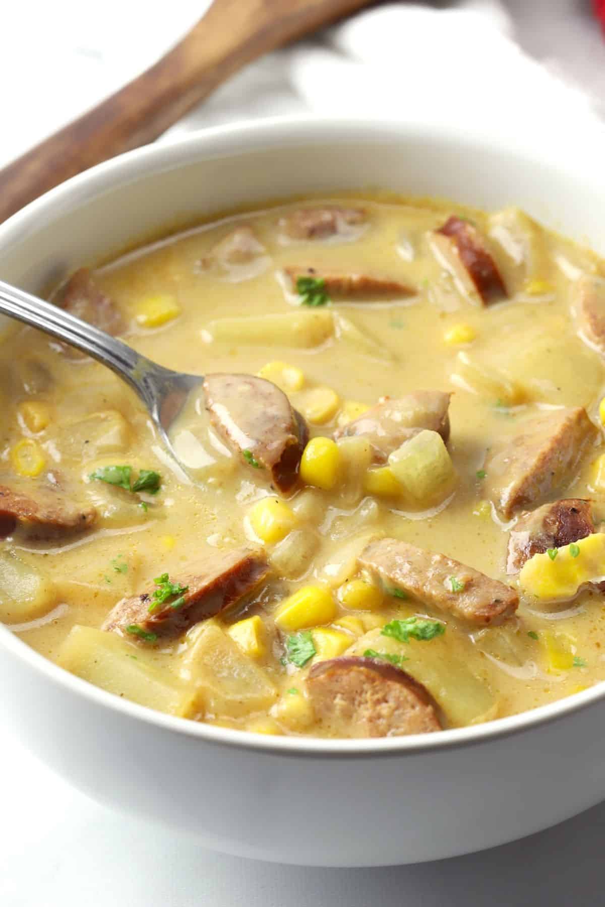 Creamy corn chowder with andouille sausage in a white bowl with a spoon.