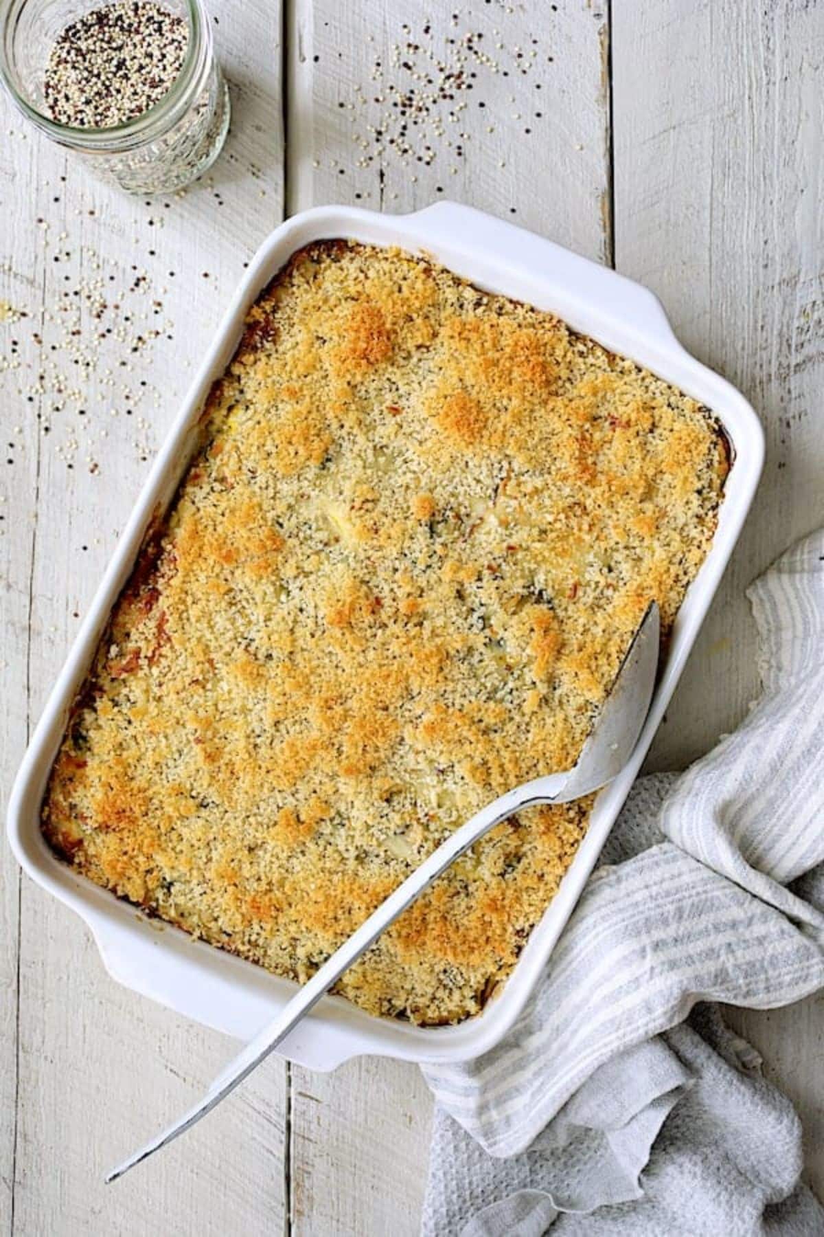 Crispy zucchini, yellow squash, and quinoa in a white casserole with a spoon.