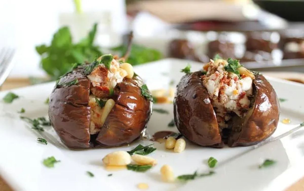 Mouth-watering roasted baby eggplants with goat cheese stuffingon a white plate.