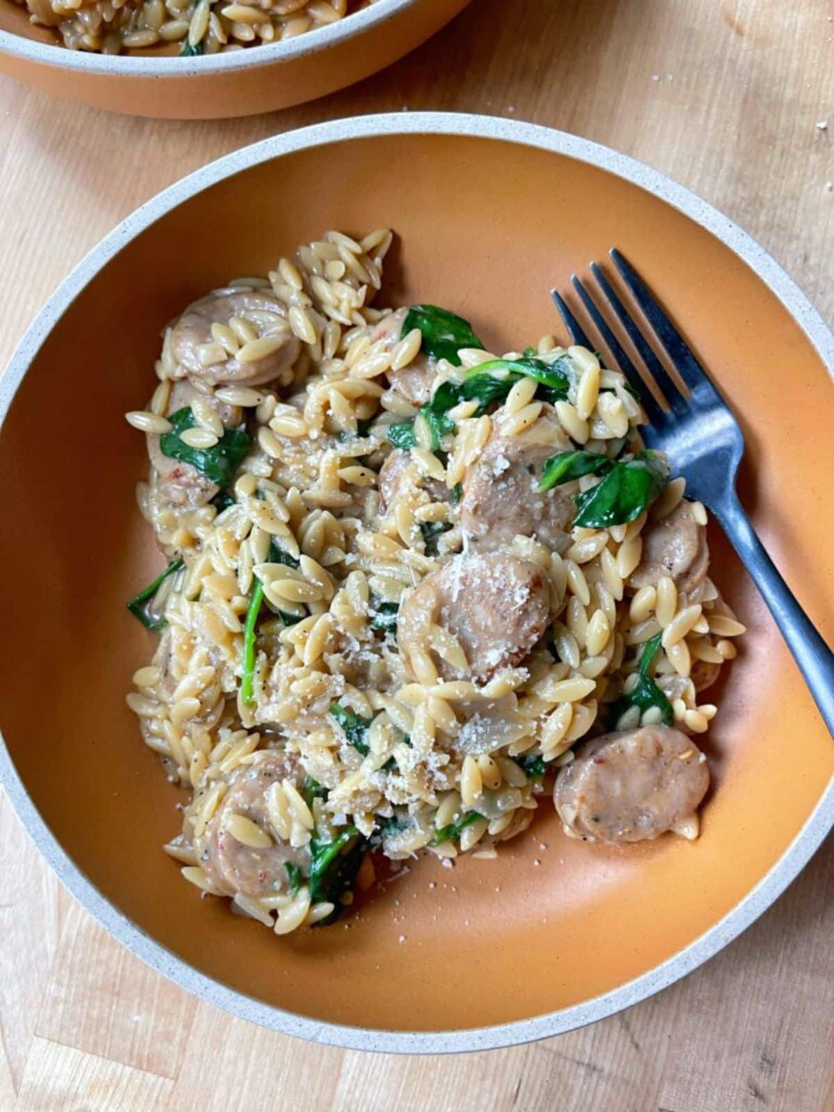 Delicious one pan chicken sausage orzoin a bowl with a fork.
