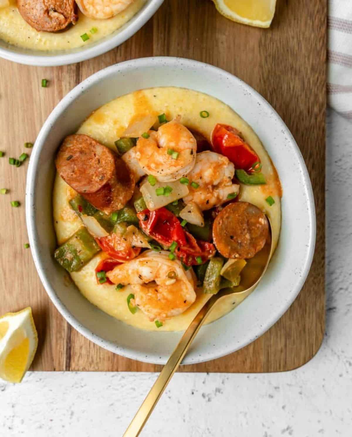 Juicy shrimp and grits with chicken sausagein a bowl with a spoon.