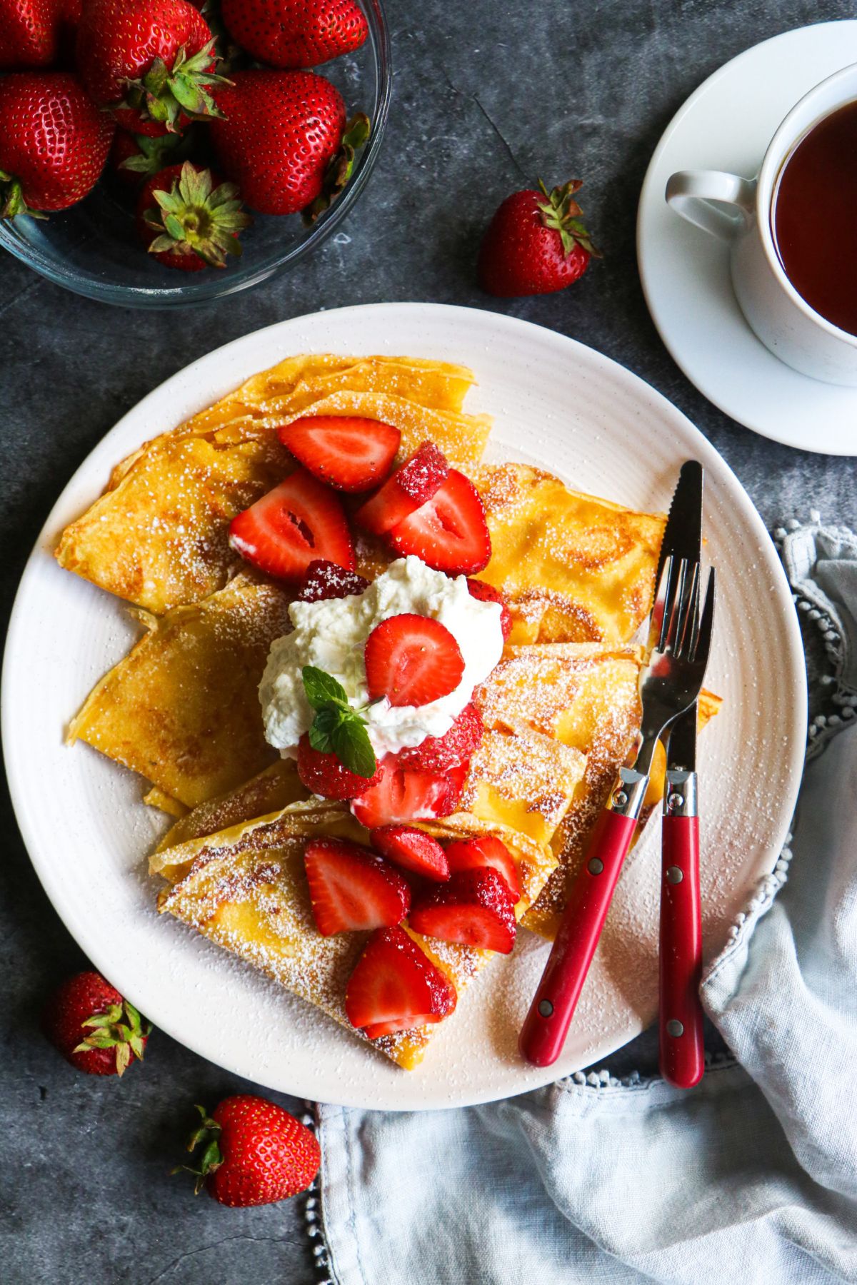 Mouth-watering strawberry crepes on a white plate with cutlery.