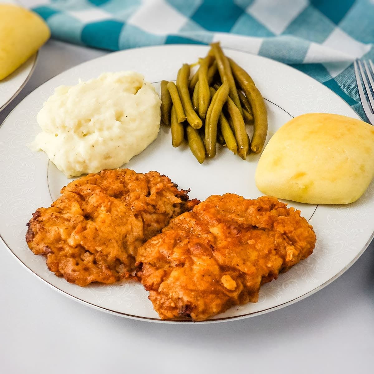 Crispy chicken fried elk steak with beans, mashed potatoes and bread on a plate.