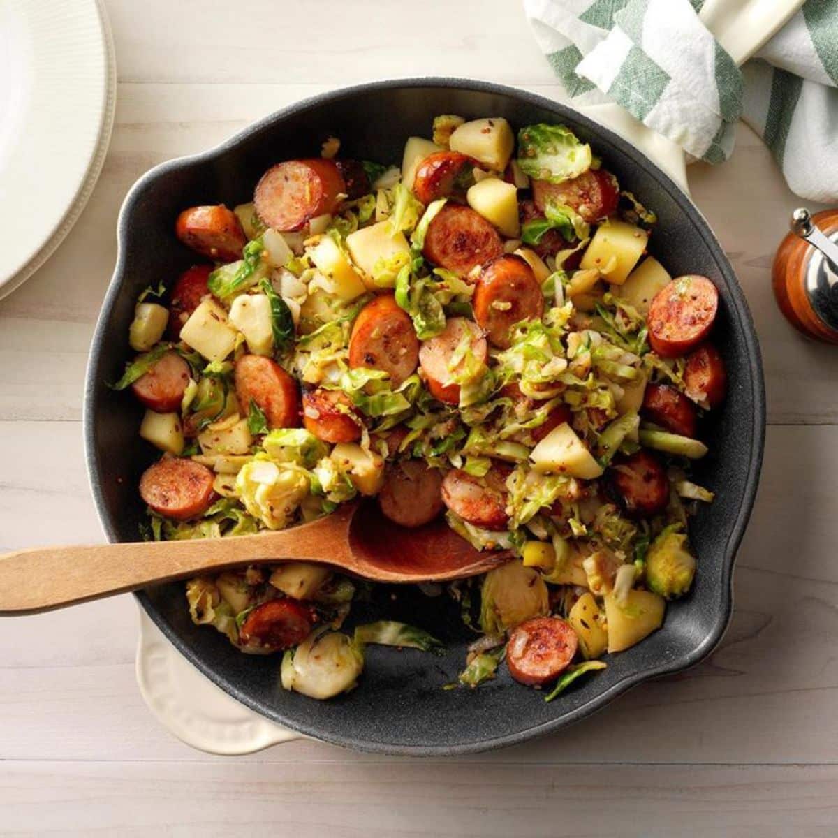 Healthy bavarian apple sausage hash in a black bowl with a wooden spoon.