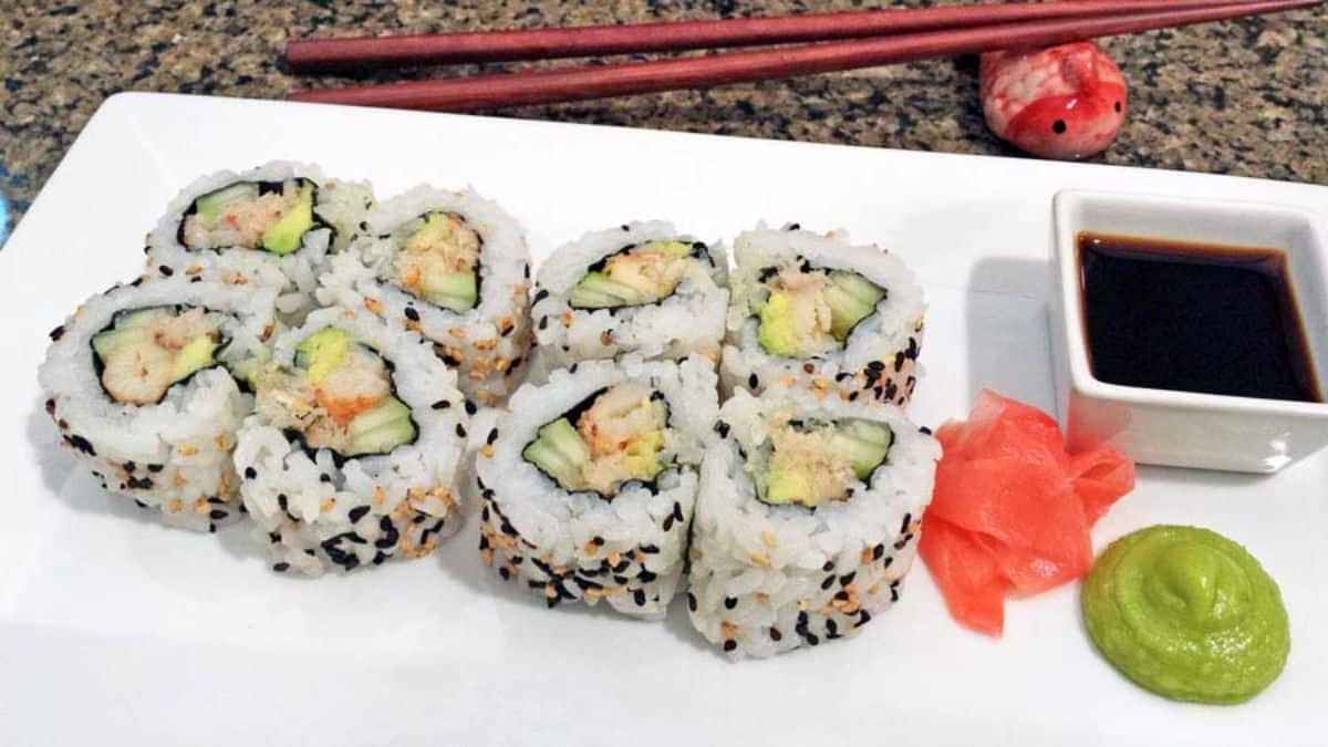 Tasty crab california rolls with a bowl of dip on a white tray.