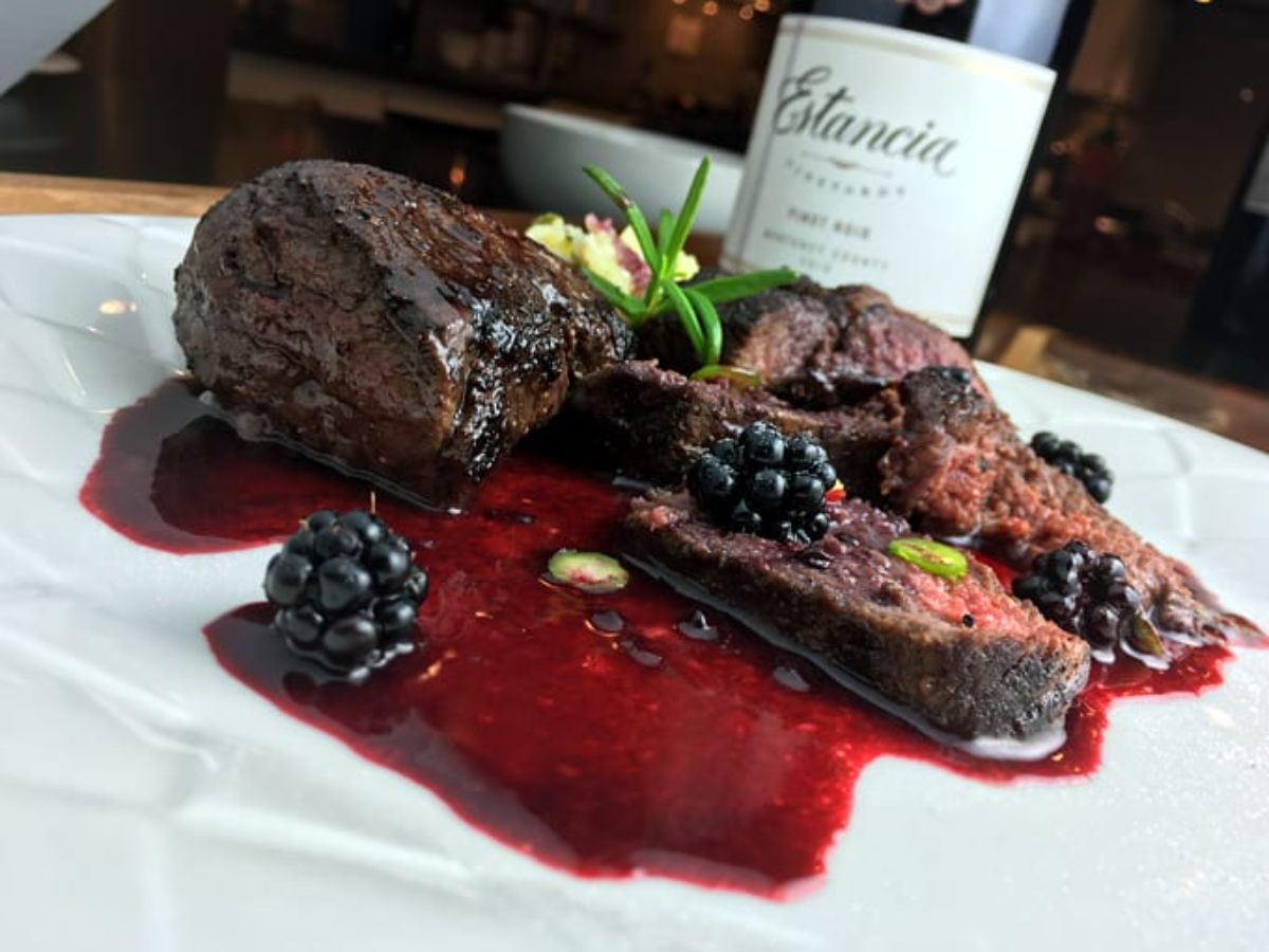 Scrumptious  elk steak medallions with blackberry red wine sauce on a white plate.