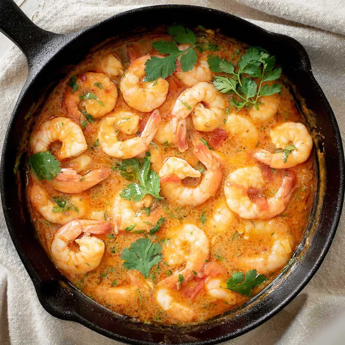 Juicy shrimp stir fry with buttery sofrito sauce in a black skillet.