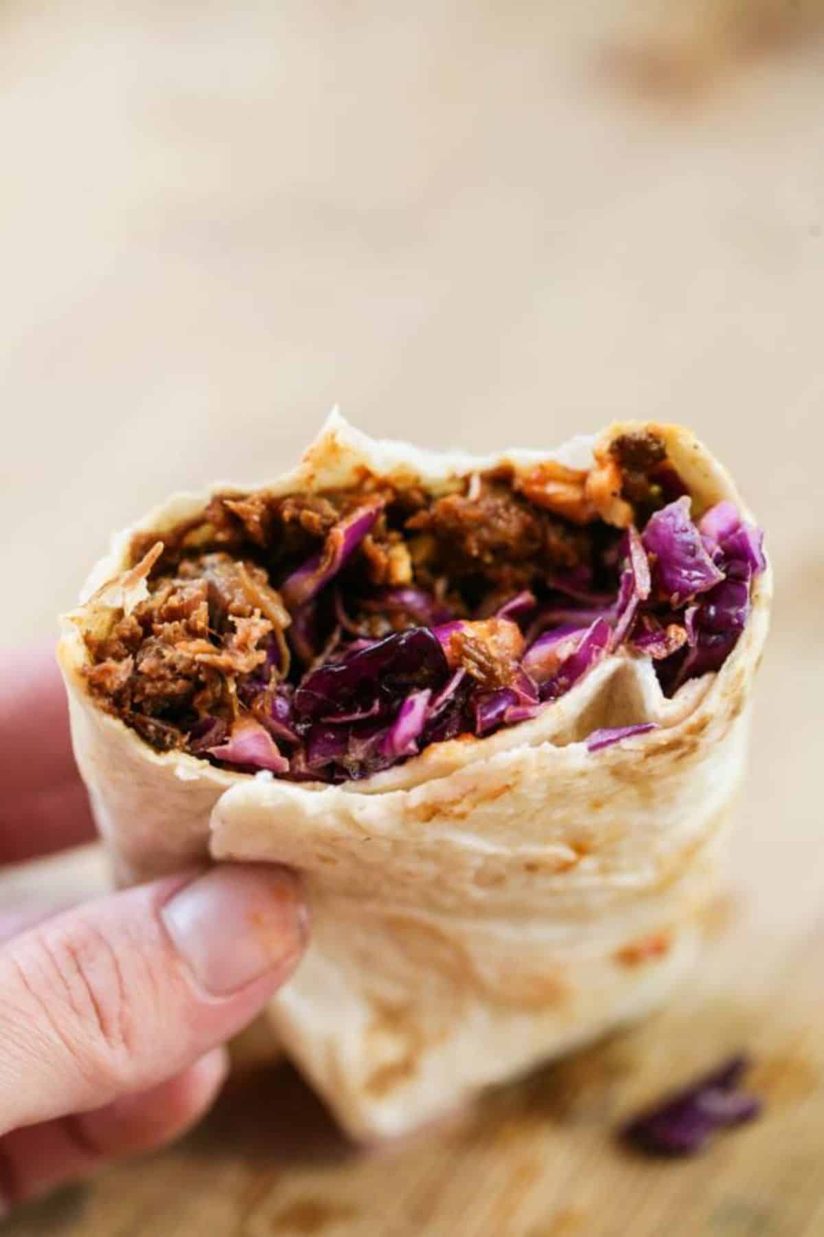 Flavorful pulled venison wrap held by hand.