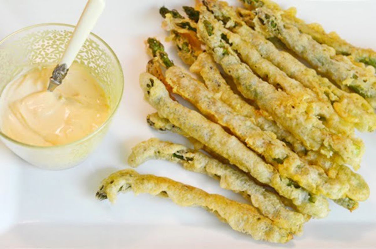 Crispy fried asparagus with a spicy dipping sauce in a bowl on a white tray.