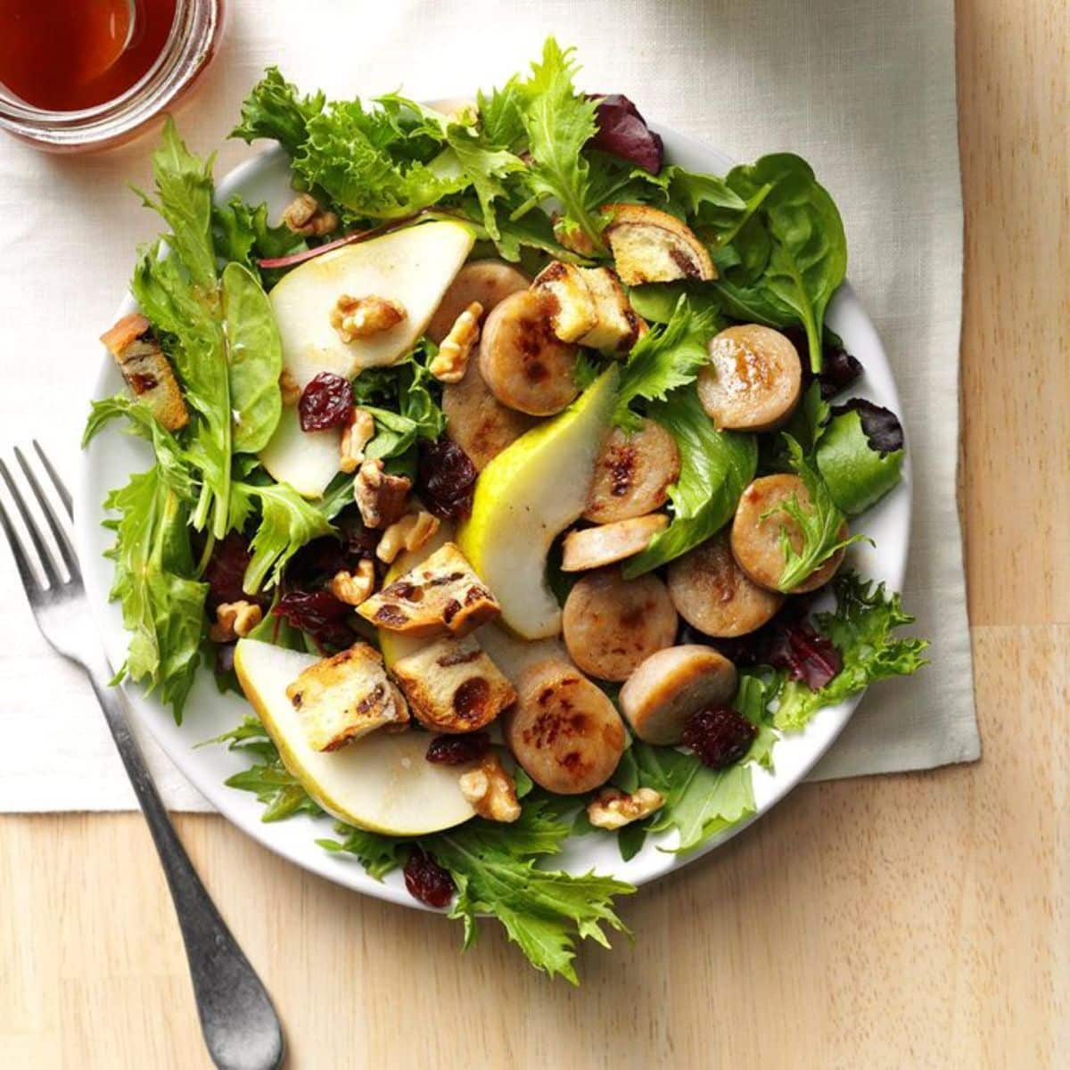 Fresh apple sausage salad with cinnamon vinaigrette on a white plate.